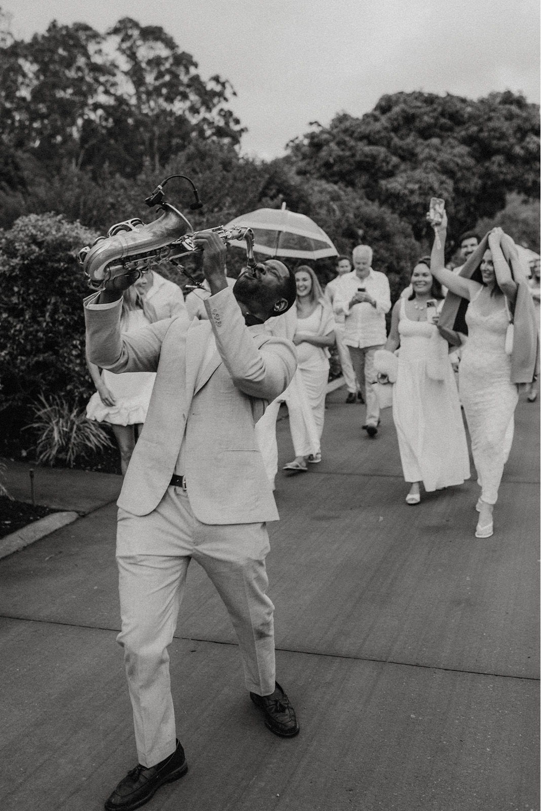 A joyful wedding procession with a man playing a saxophone and guests celebrating.
