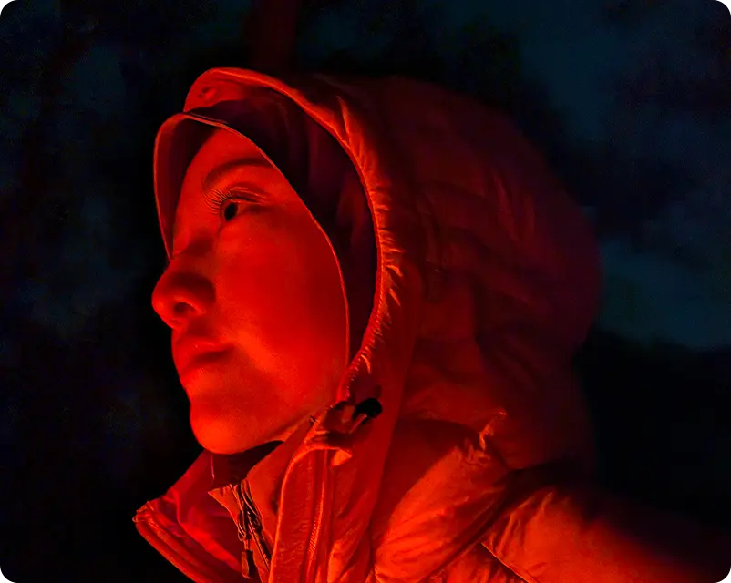A person in a hooded jacket illuminated by red light at night.
