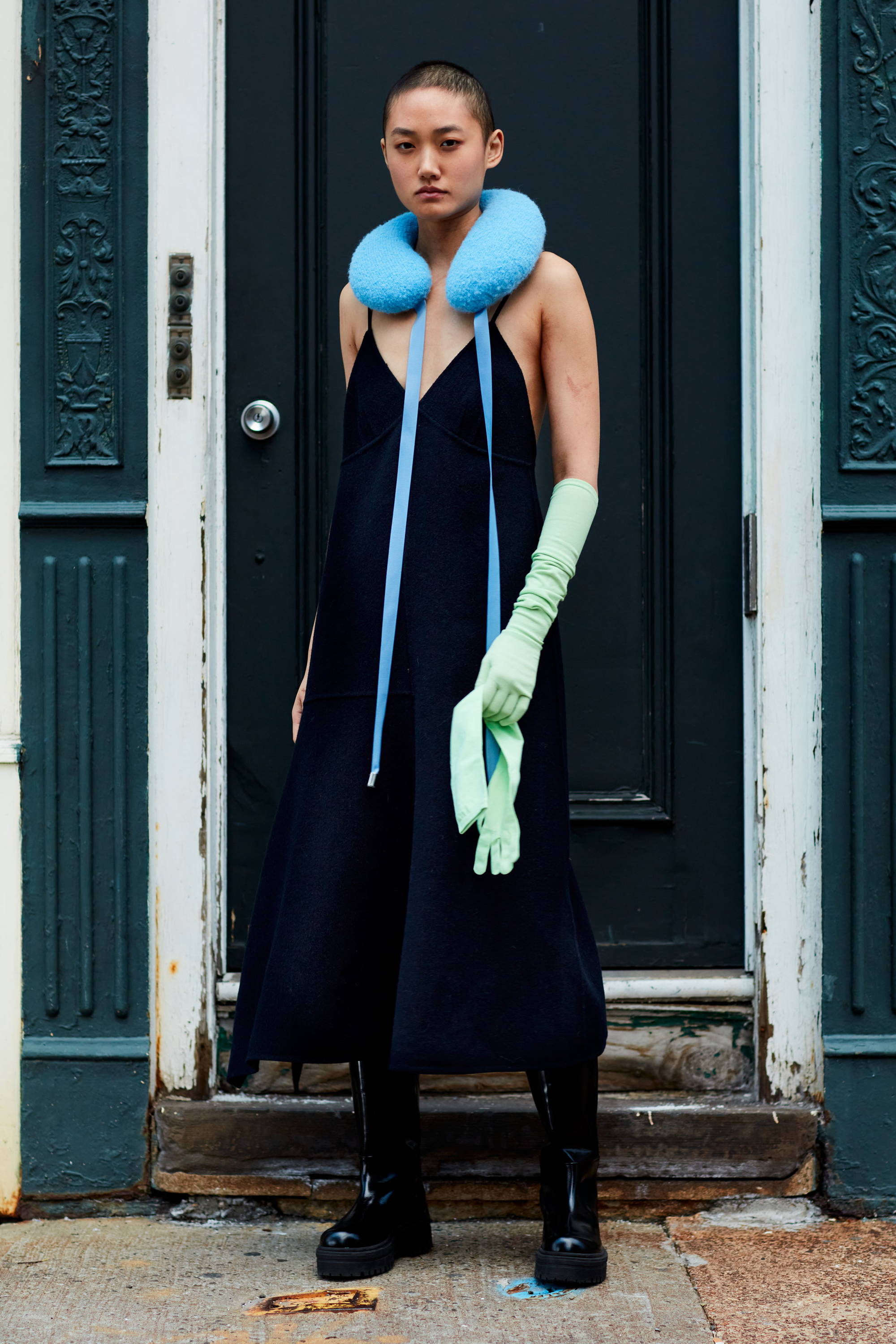 Model wearing a black dress, blue neck accessory, and green gloves.