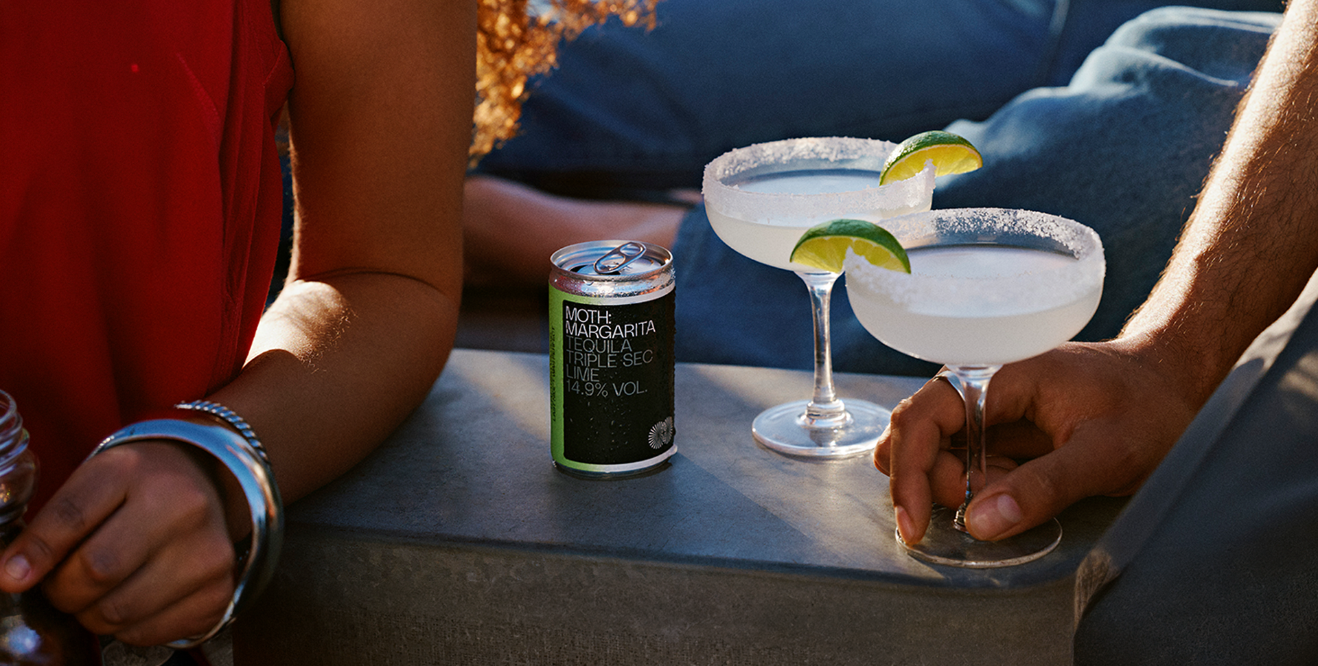 Two margaritas with lime garnishes and a can on a table.