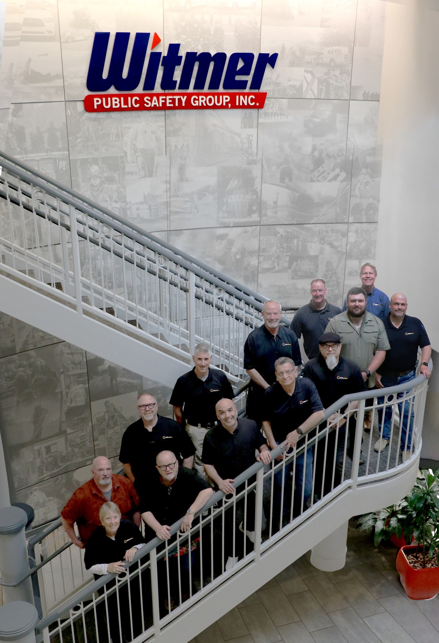 Group of people posing on a staircase with a company logo.