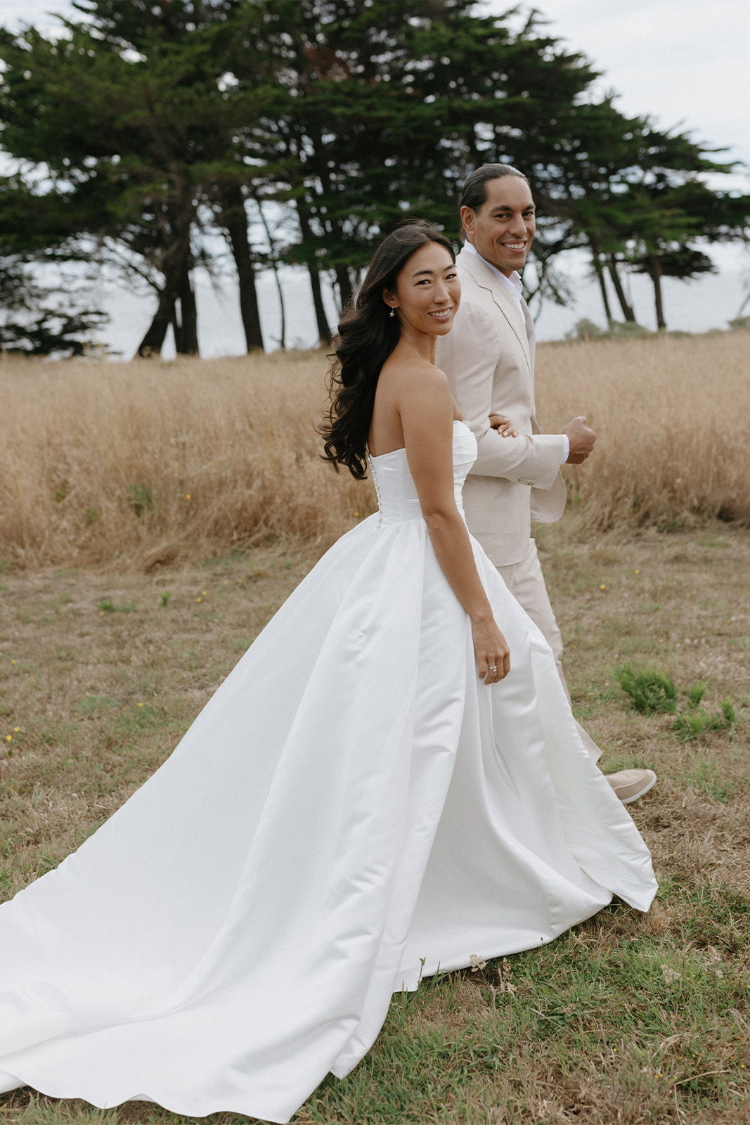 Bride and groom walking together in a grassy field.
