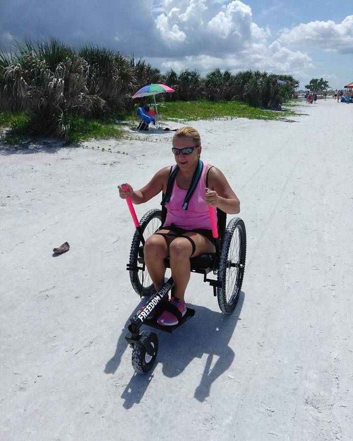 Adult pushing levers of GRIT Freedom Chair all-terrain wheelchair on beach sand