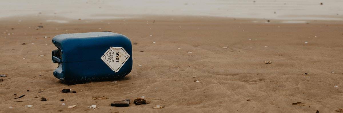 A plastic bottle with a toxic label lying alone on a sandy beach near the water