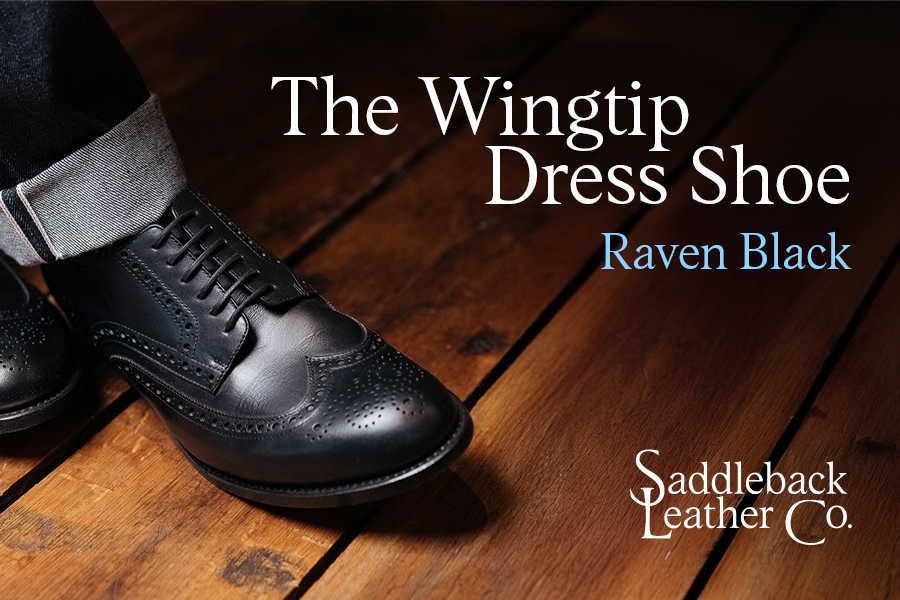A black wingtip dress shoe on a wooden floor.
