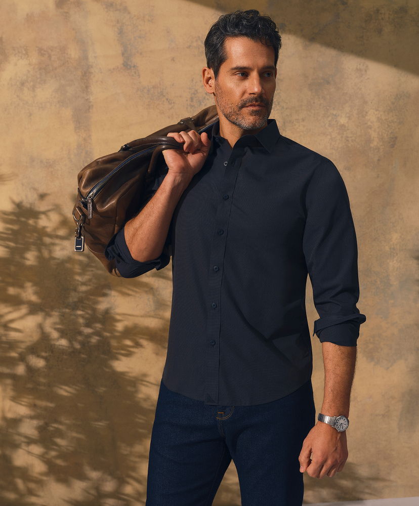 Man in a dark shirt holding a jacket against a textured background.