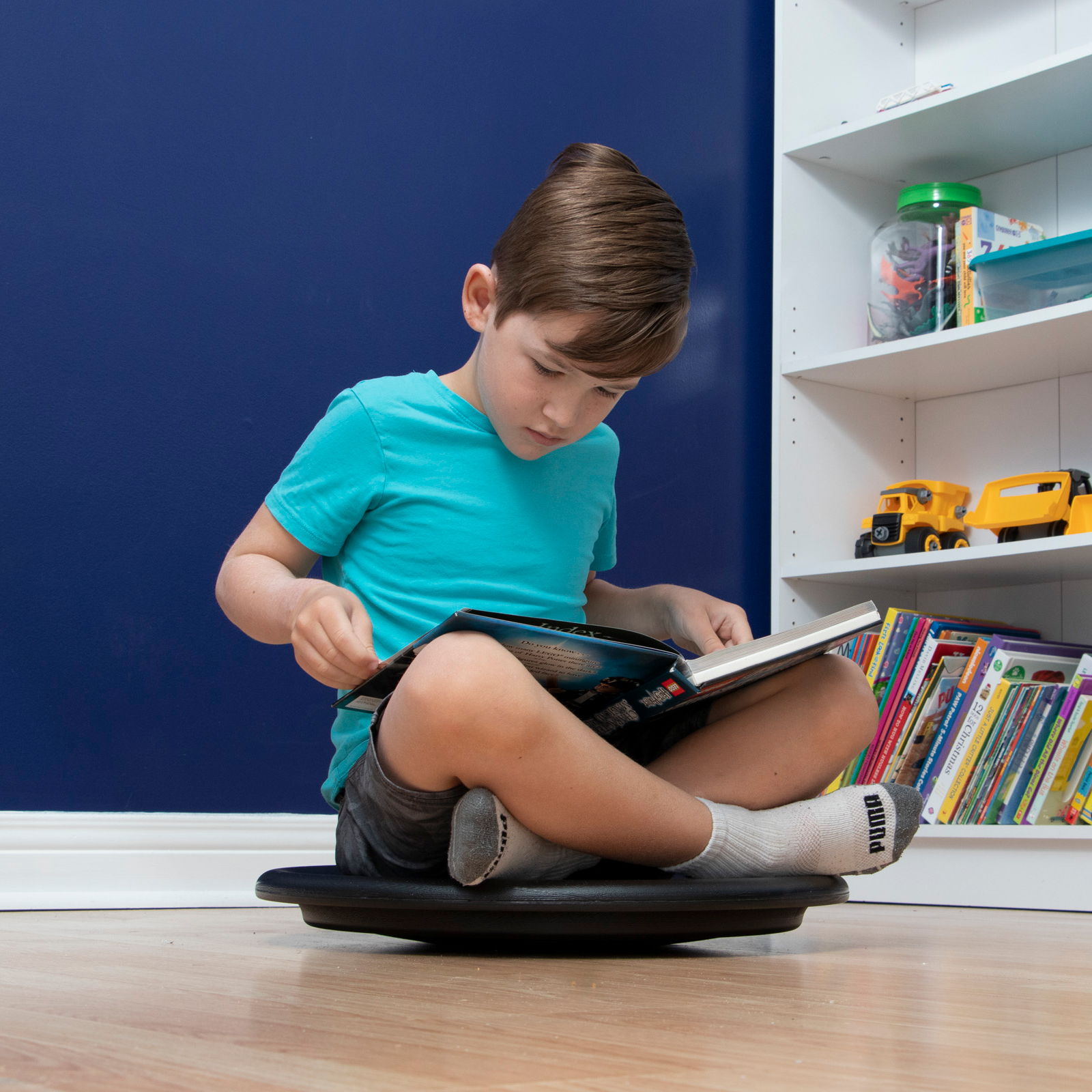 Boy reading a book on a black floor wobble balance disc