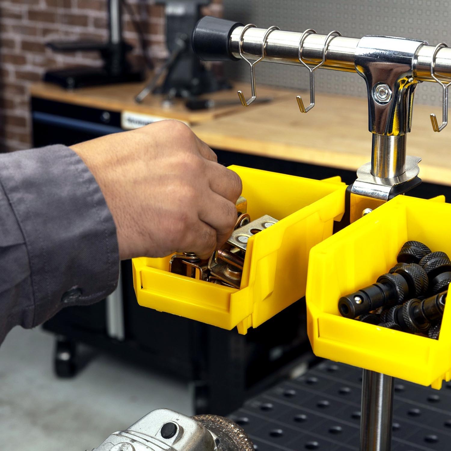 Hand reaching into yellow storage bins filled with tools in a workshop.