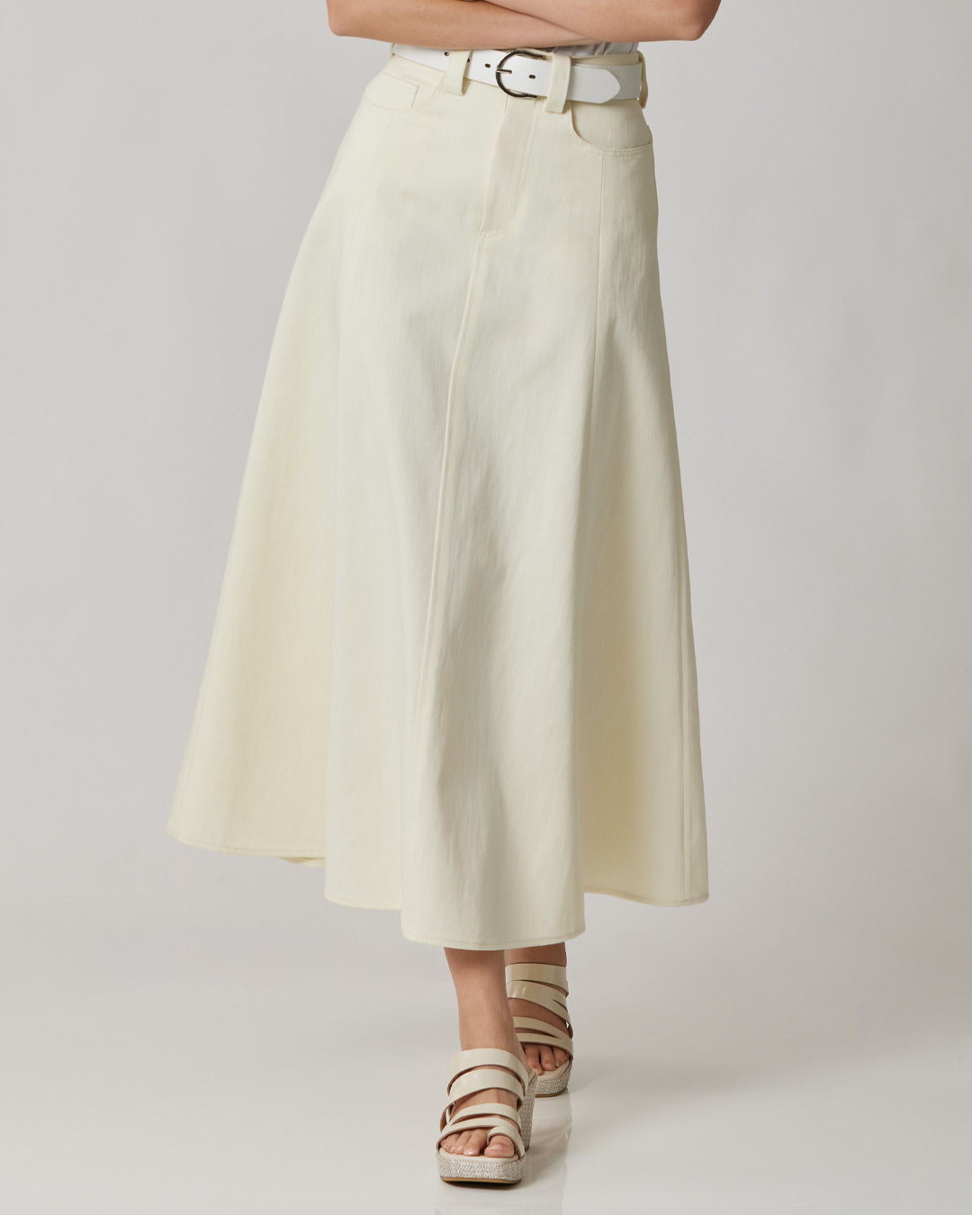 A person wearing a long, cream-colored skirt and white sandals.