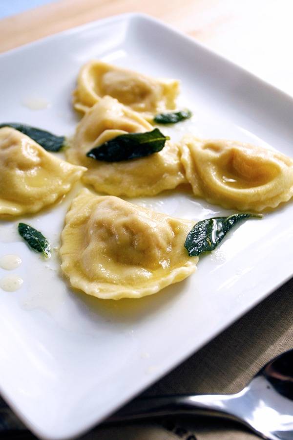 Cooked ravioli in an oily sauce garnished with sage leaves and served on a plate