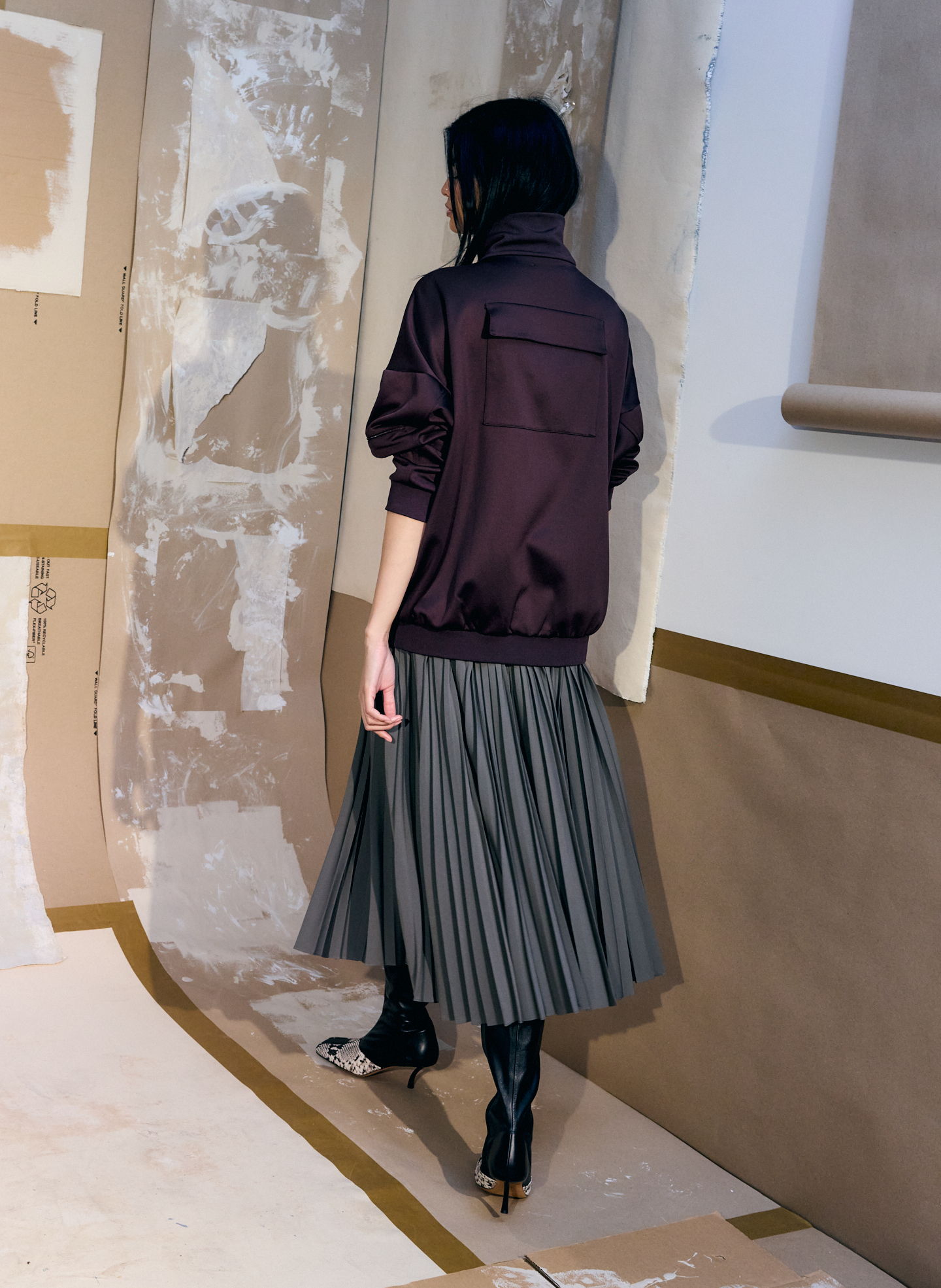 A person wearing a dark jacket and pleated skirt, viewed from behind.