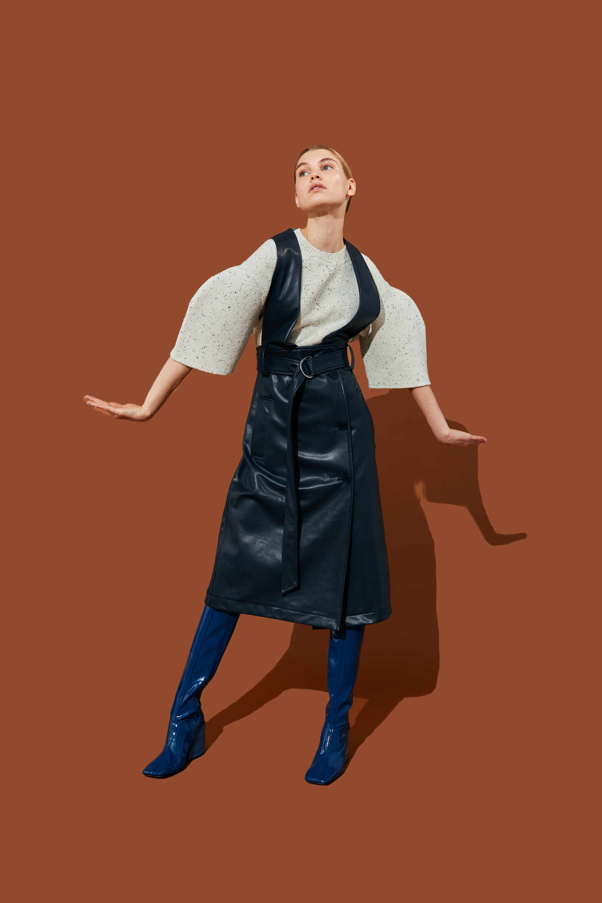 A model poses in a stylish outfit against a brown background.