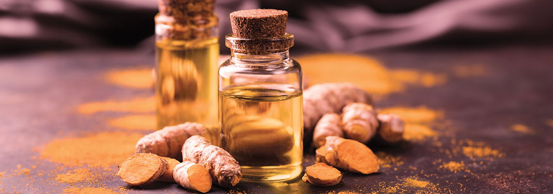 Bottles of oil surrounded by turmeric roots and powder on a dark surface.