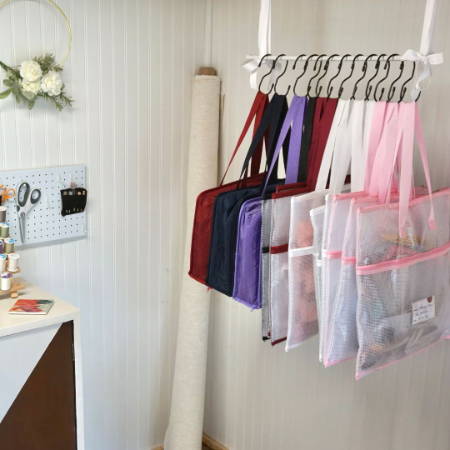 a lot of project bags and zipper binder bags hanging on a rod in a sewing room