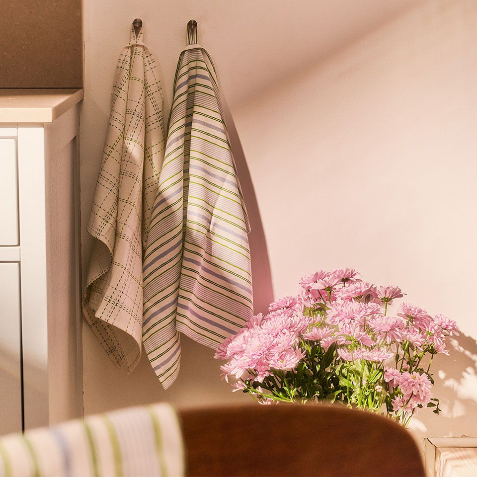 Two striped kitchen towels hanging next to a vase of pink flowers.