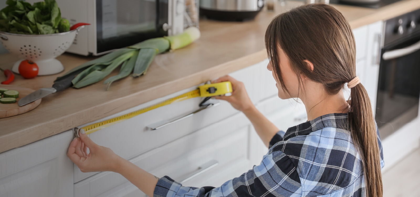 Person measuring a kitchen countertop with a tape measure.