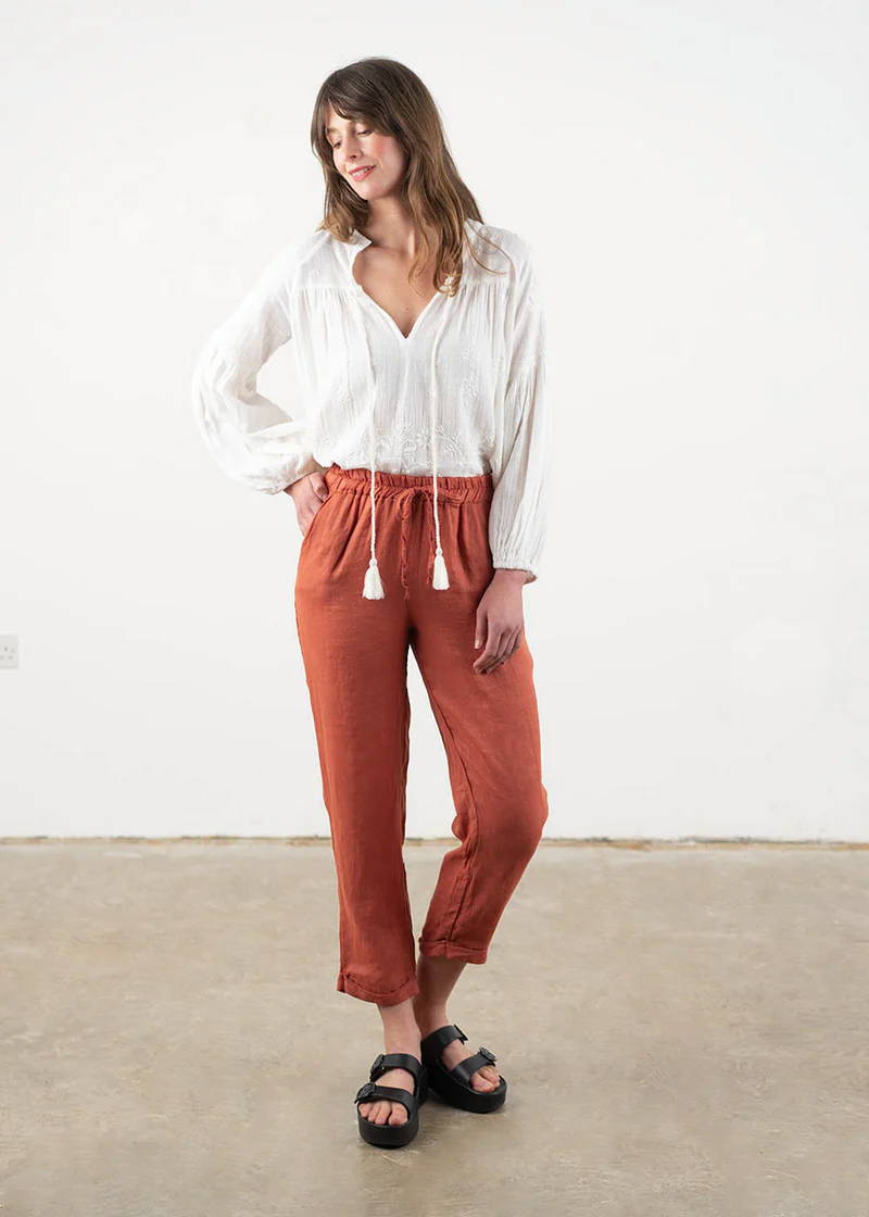 A model wearing a white, bohemian style long sleeved blouse with terracotta coloured tapered cotton trousers and black platform slides