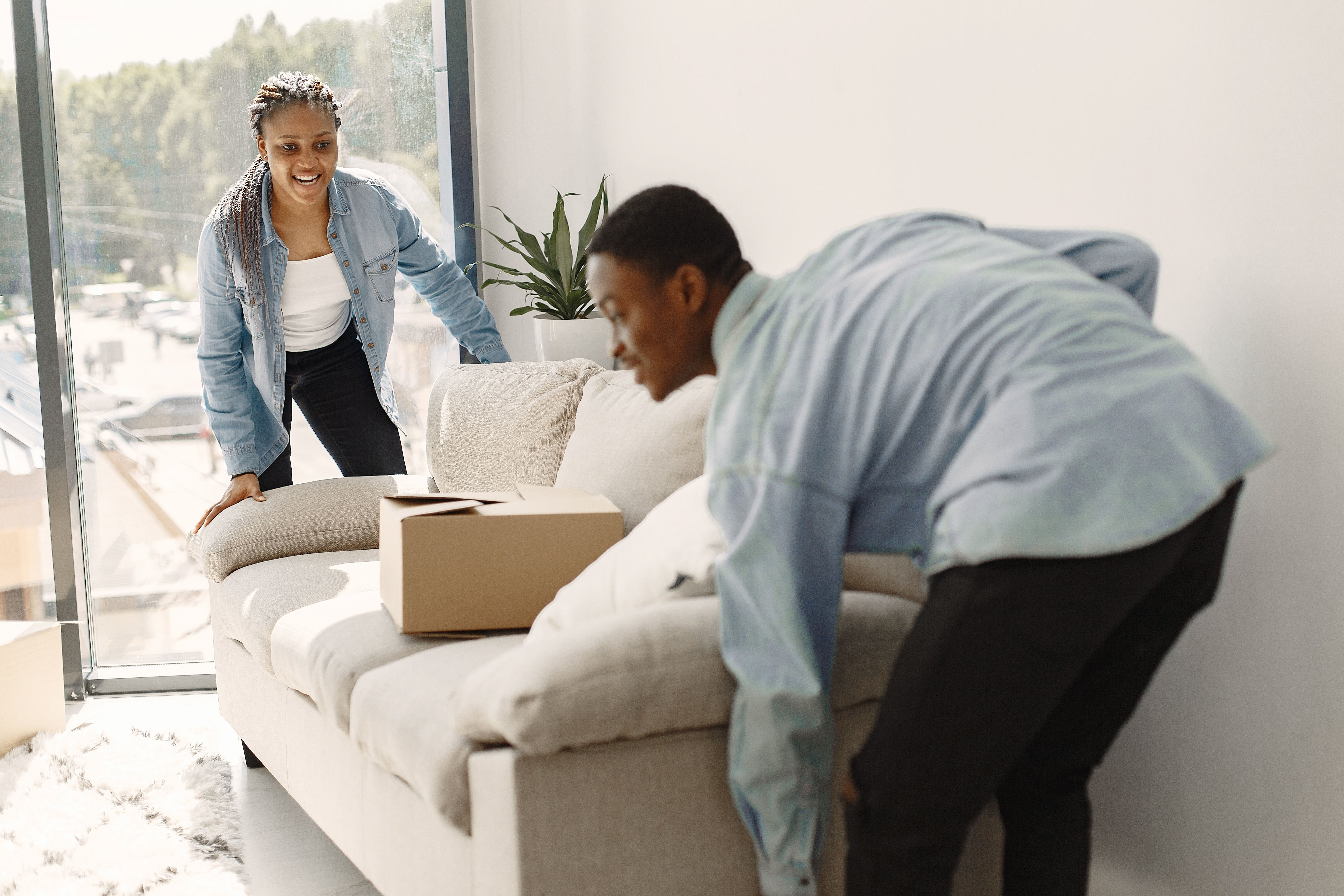 Two people interacting in a bright living room with a package on the sofa.