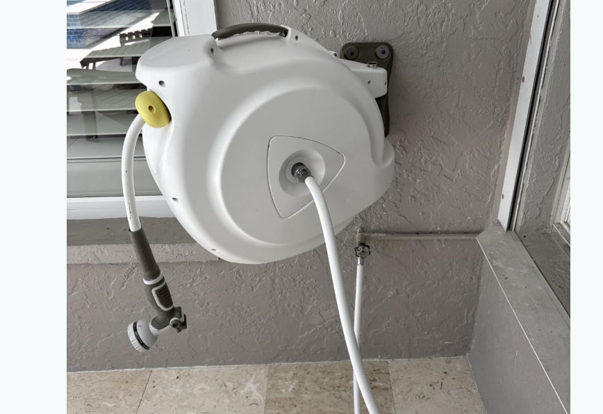 White wall-mounted hose reel with a hose extending from it.