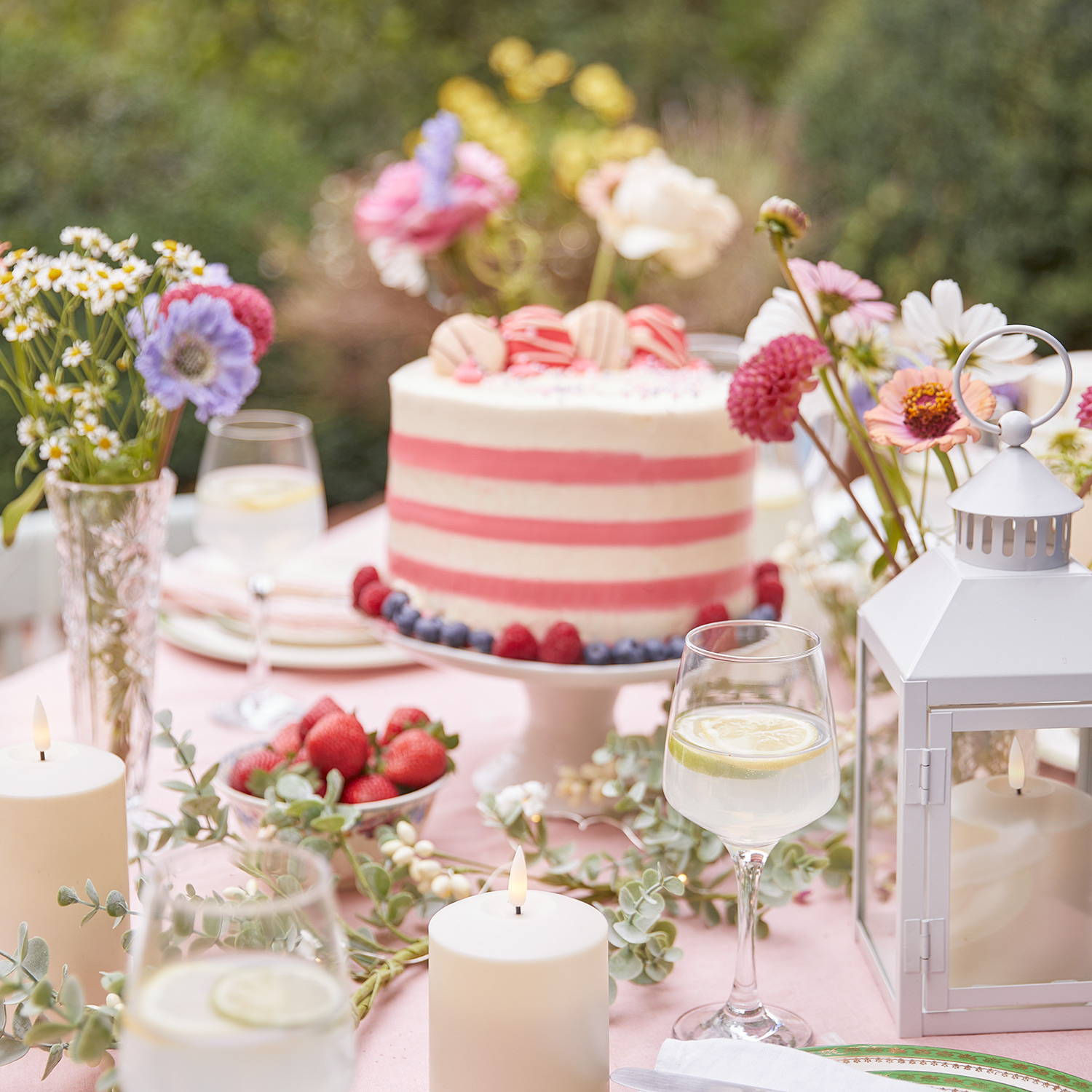 A close up of an outdoor dining table with cakes, sweet treats and LED candles.