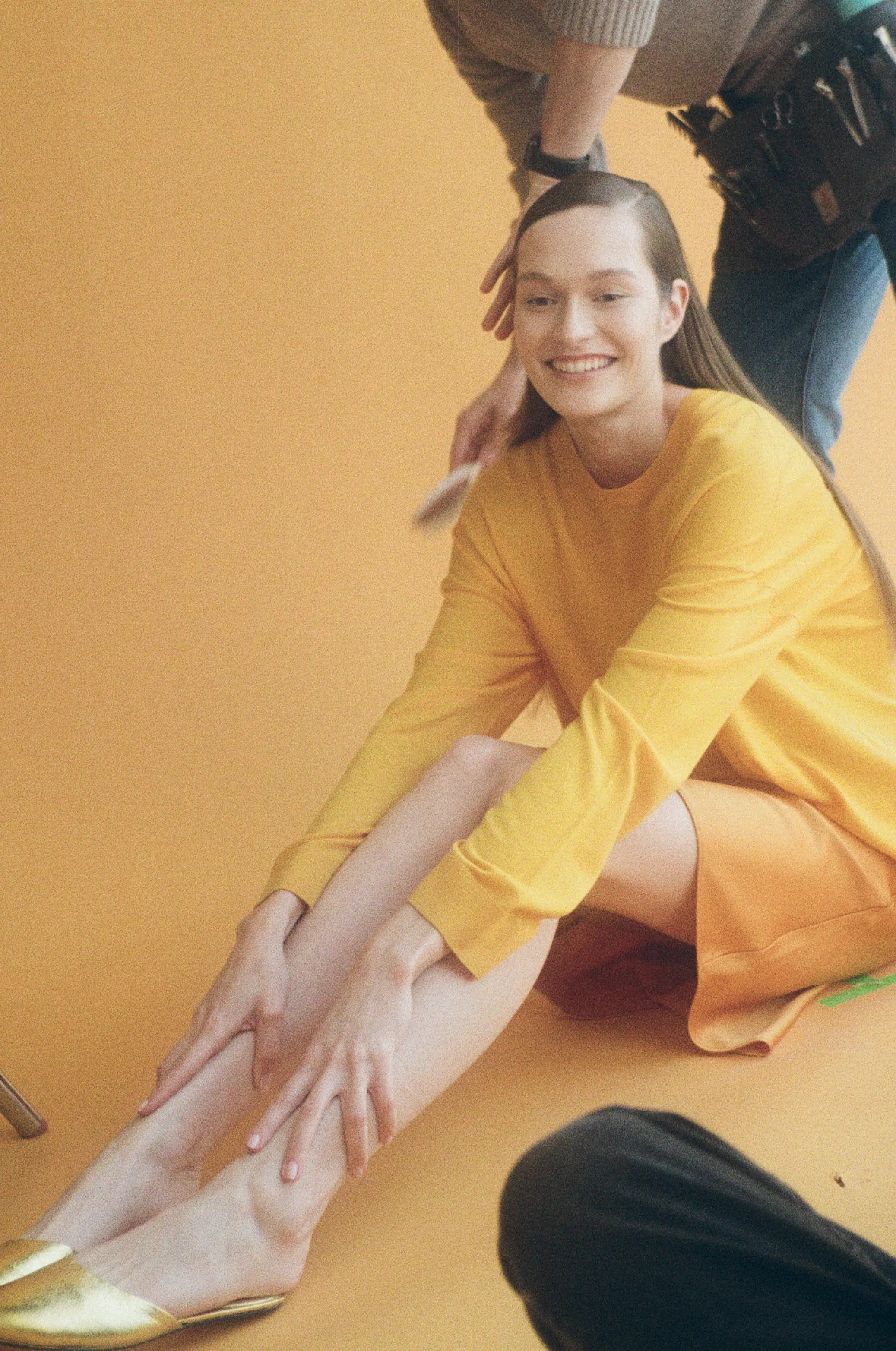 Woman on ground with hands on legs, smiling with someone brushing hair
