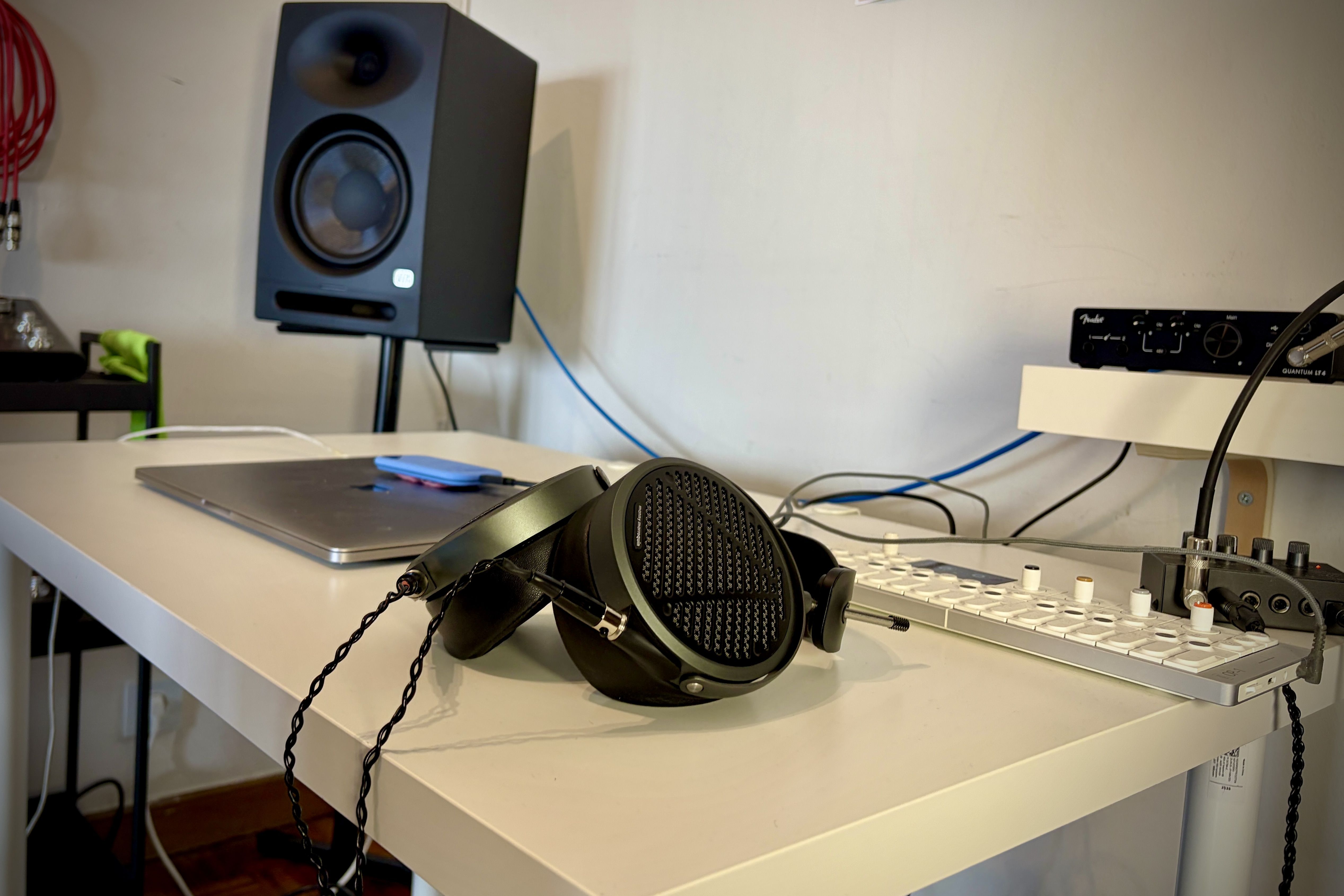 Audeze MM-500 headphones on a desk with audio equipment and a speaker in the background.