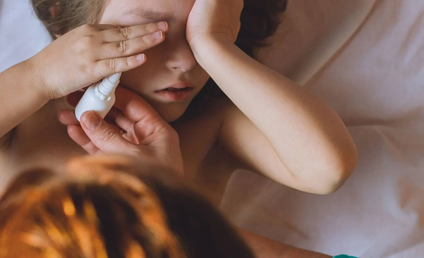  Ein Mädchen hält sich die Hände vors Gesicht, während ihre Mutter ihr Allergie-Augentropfen gibt, um den Juckreiz zu lindern