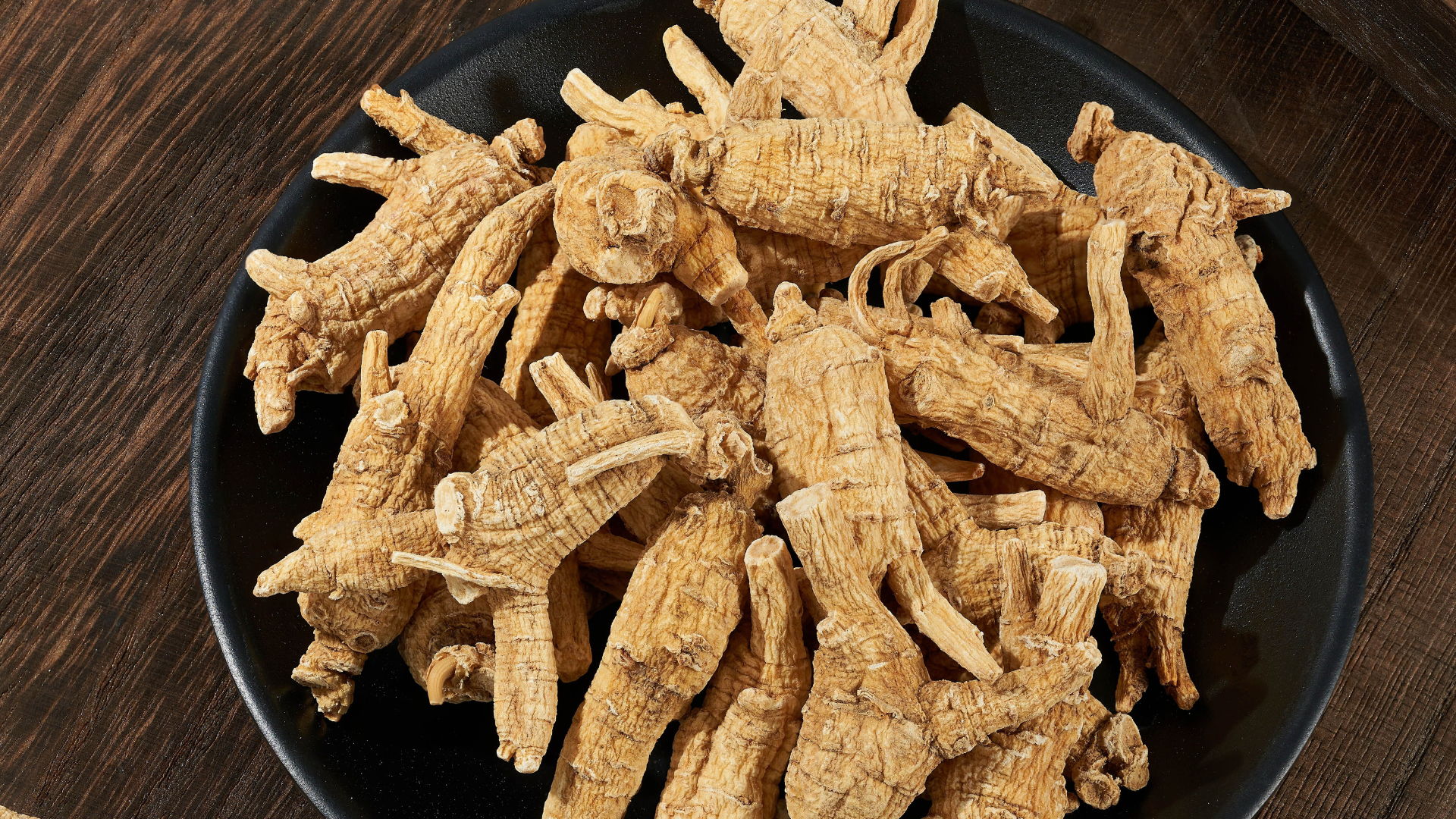 A bowl of dried ginseng roots on a wooden surface.
