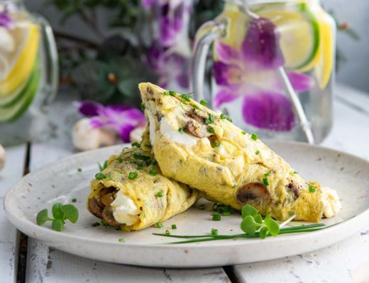 Two omelettes garnished with herbs on a plate, with drinks in the background.