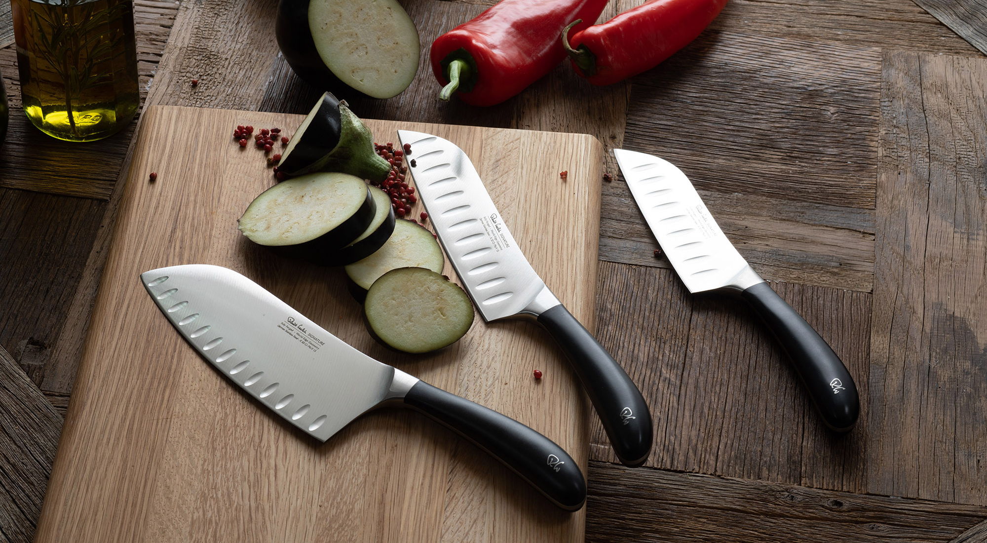 Three Signature Santoku Kitchen Knives on a wooden cutting board with sliced vegetables.
