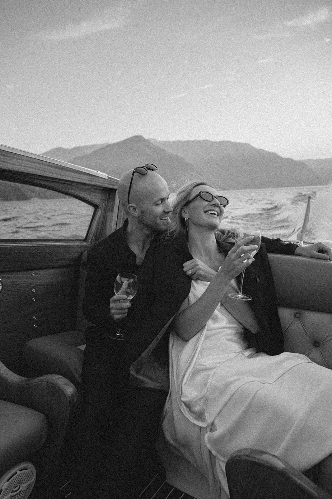 Couple enjoying drinks on a boat, surrounded by mountains and water.