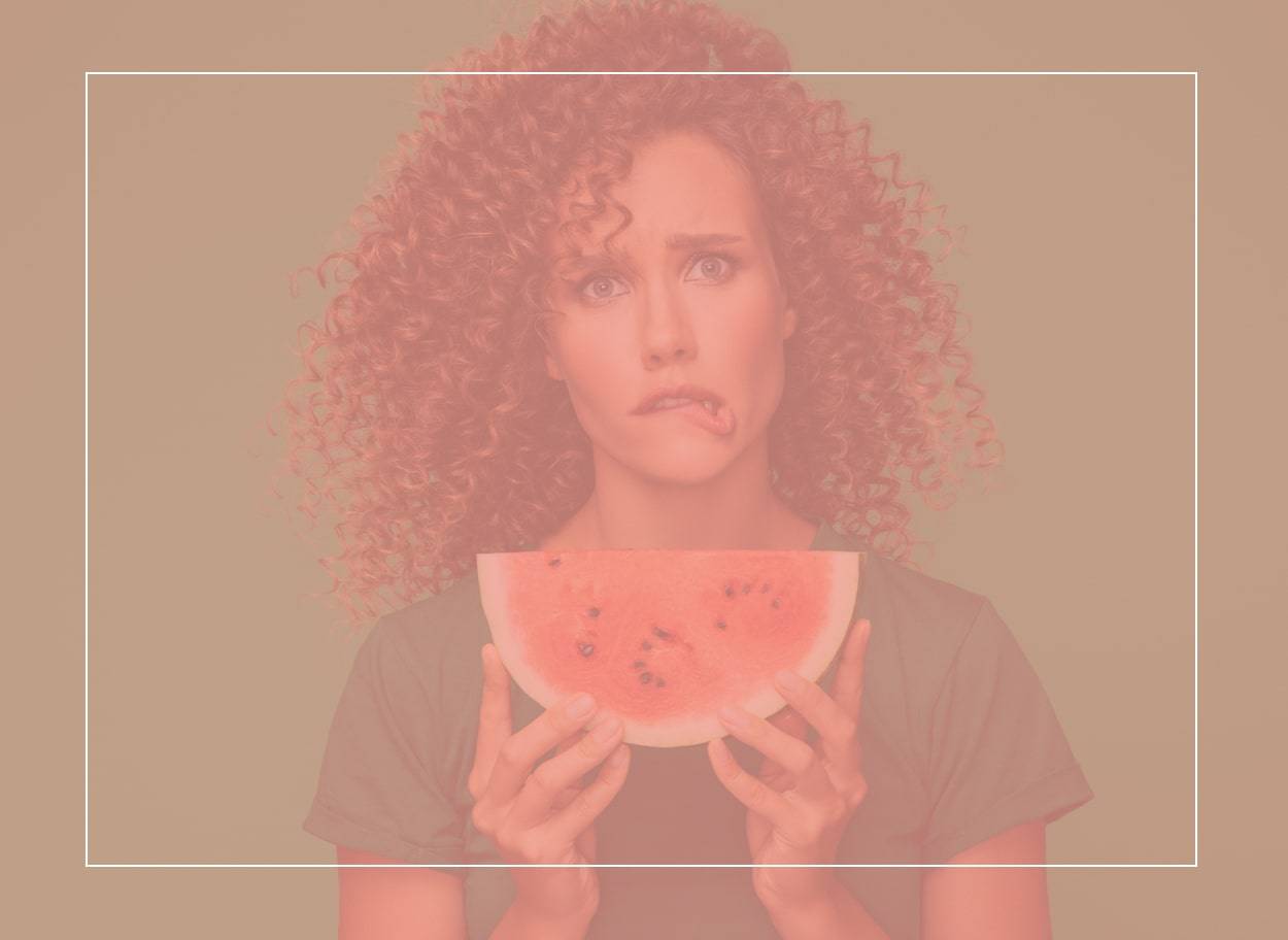 Une femme tient une tranche de melon d’eau juteuse et se mord la lèvre. Des picotements dans la bouche peuvent être un symptôme du syndrome pollen-aliment.
