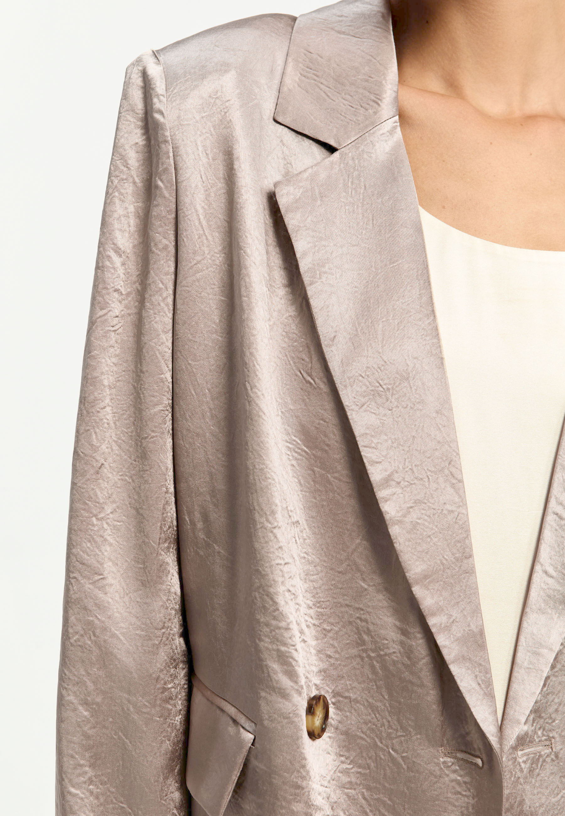 Close-up of a light-colored satin blazer with a button.
