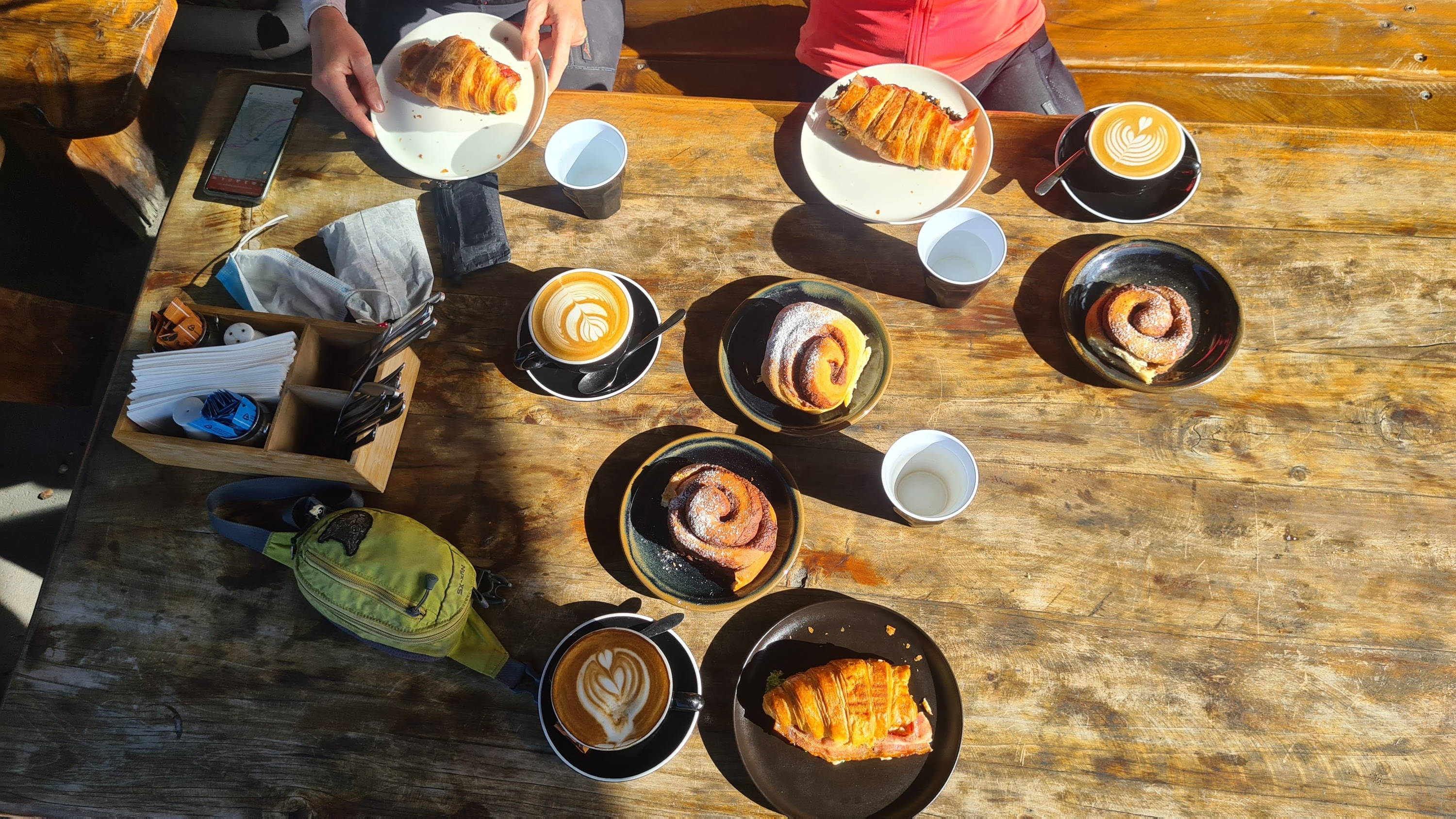 A warm breakfast of croissants, lattes, and sweet buns are laid out on a wooden table.