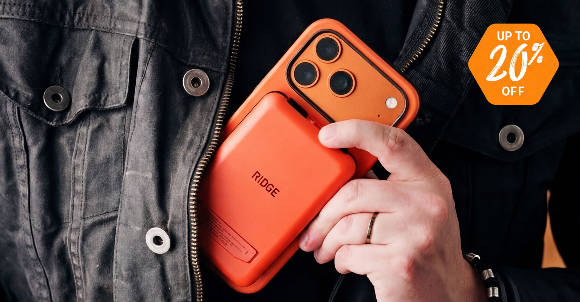 Person holding an orange phone and power bank, wearing a black jacket.
