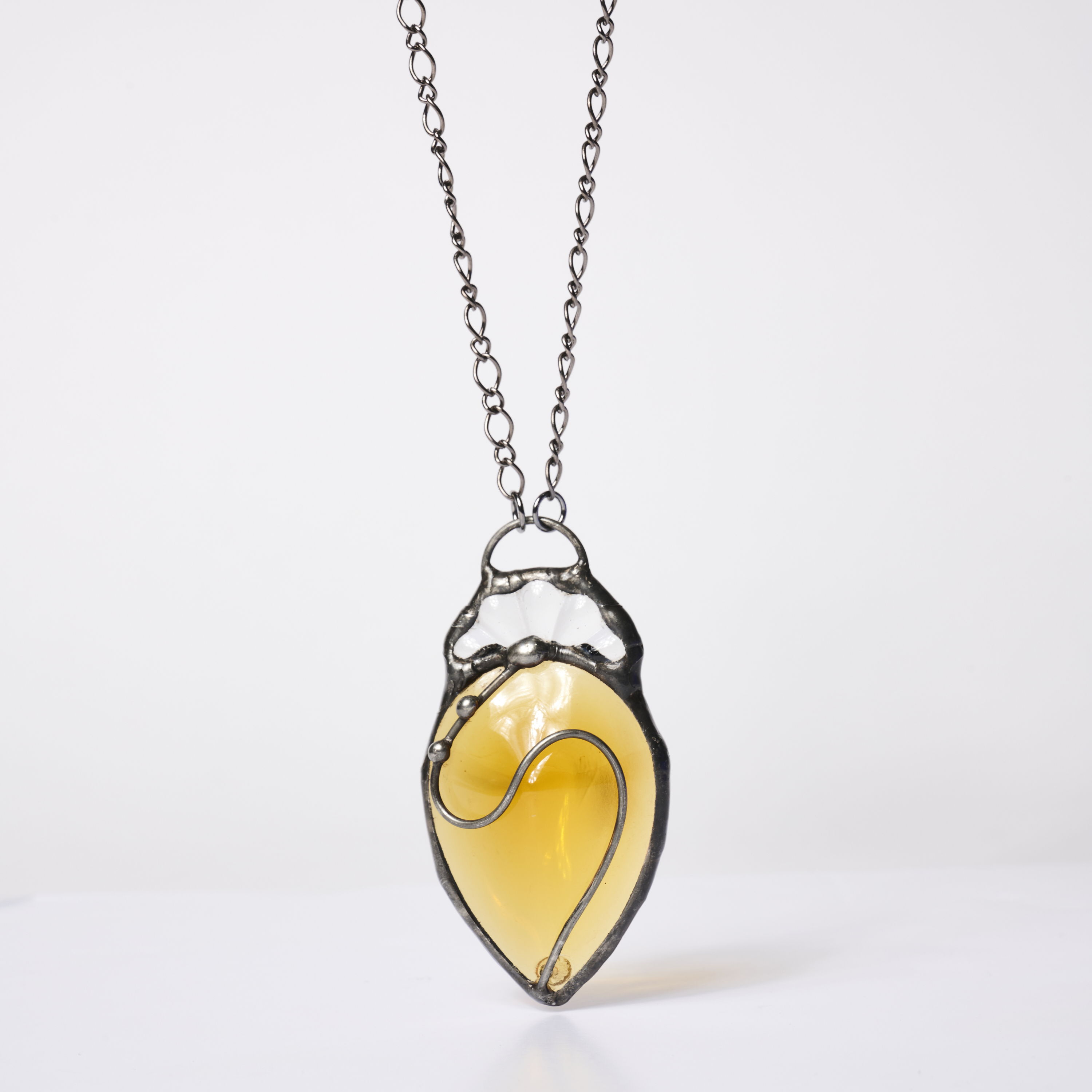 A yellow glass pendant in a metal frame on a chain necklace.