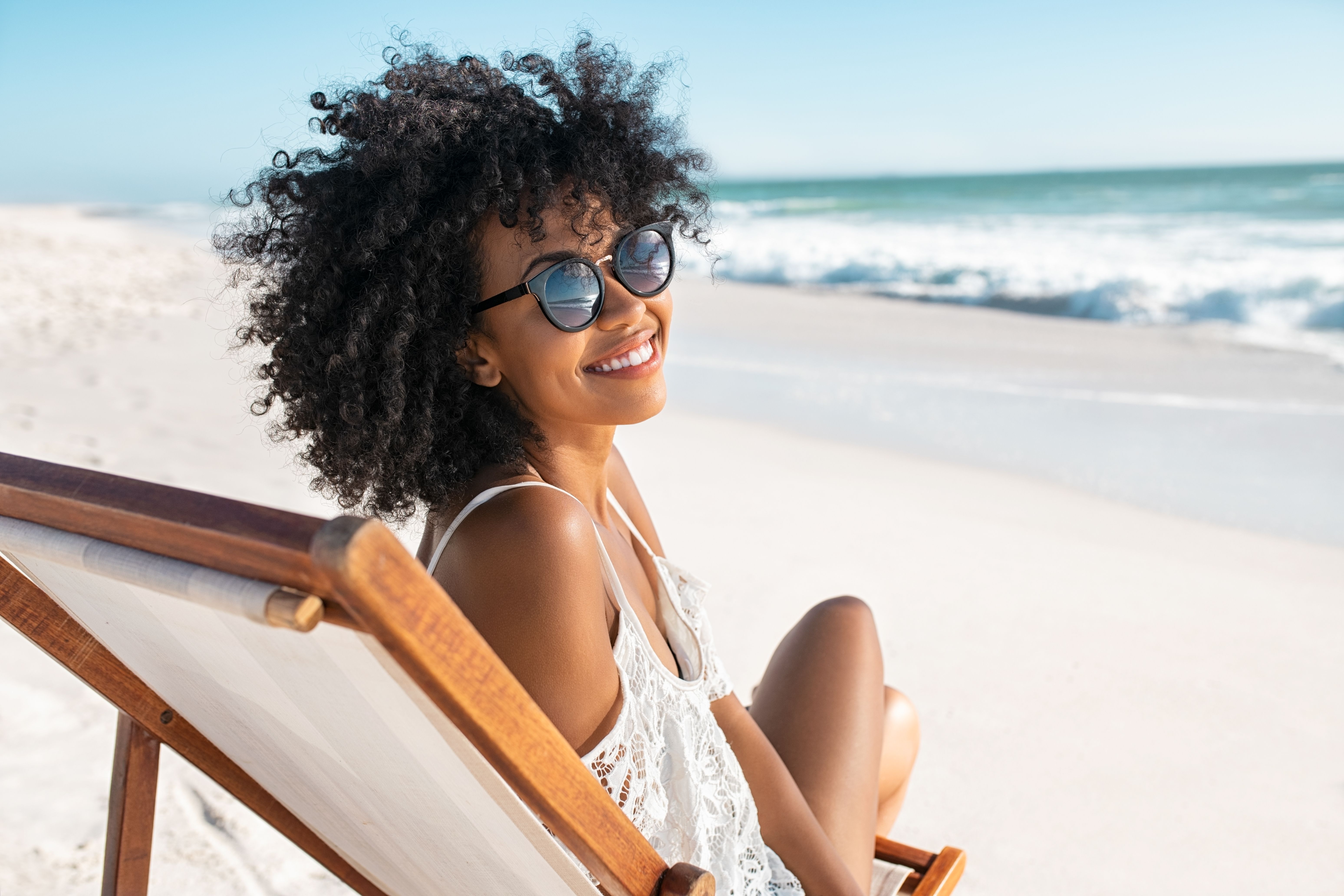Smiling woman in sunglasses relaxing on the beach by the ocean.