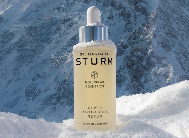 A skincare serum bottle on snow with mountains in the background.