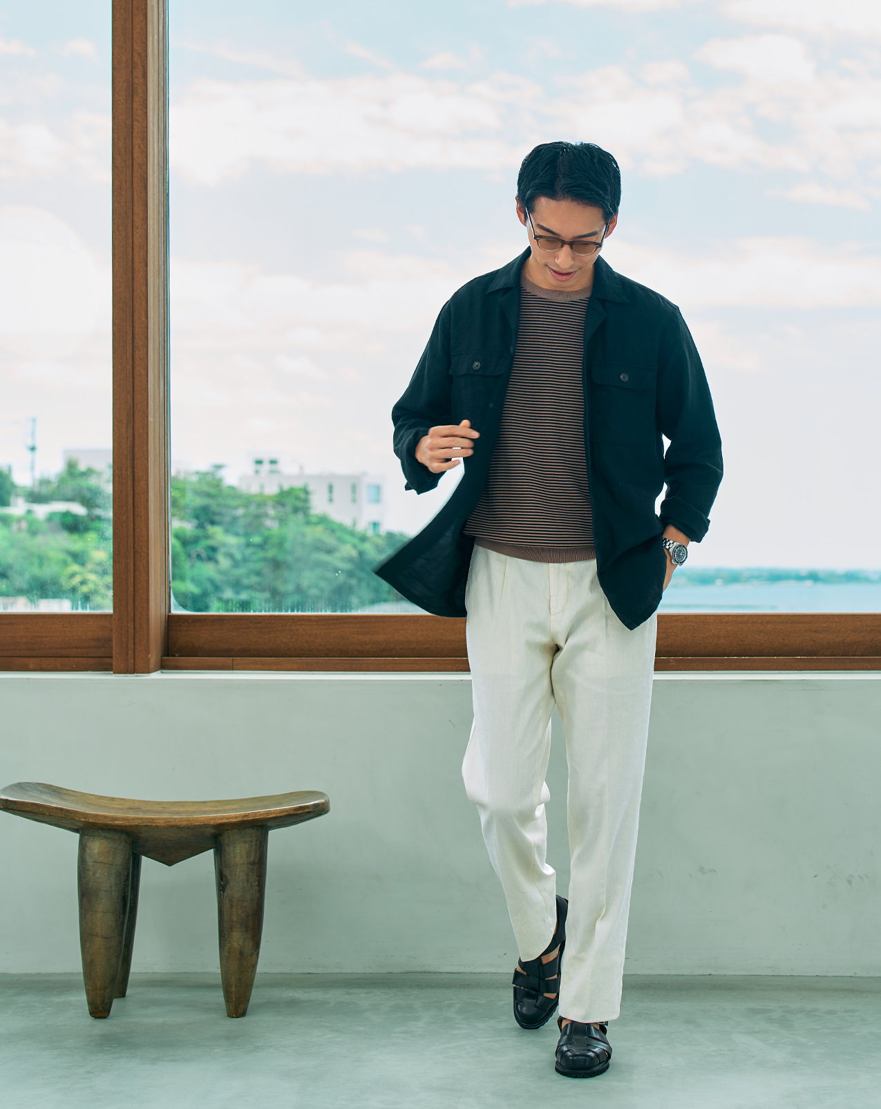 A man walking indoors near a large window with greenery outside.