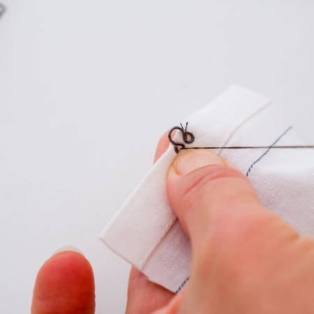 Part of a hook and eye closure being sewn to a piece of fabric 