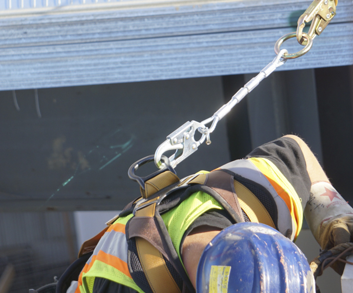 Ironworker bending down that has a cable D-ring extender and a leading edge lanyard attached to his harness