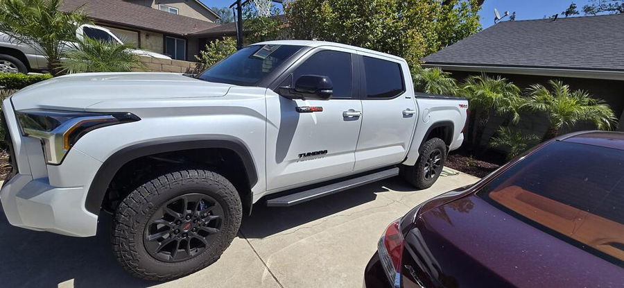 Front-three-quarter view Dirk's white 2026 Toyota Tundra TRD Off-Road with black wheels and off-road tires in residential driveway HornBlasters Stealth Spare Tire Delete featured install gallery photo 1