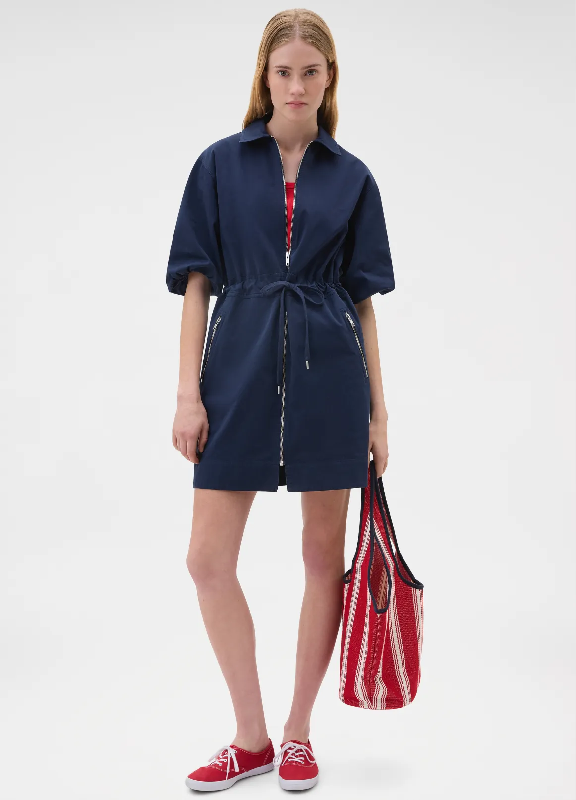Model wearing a navy dress with a red bag and sneakers.