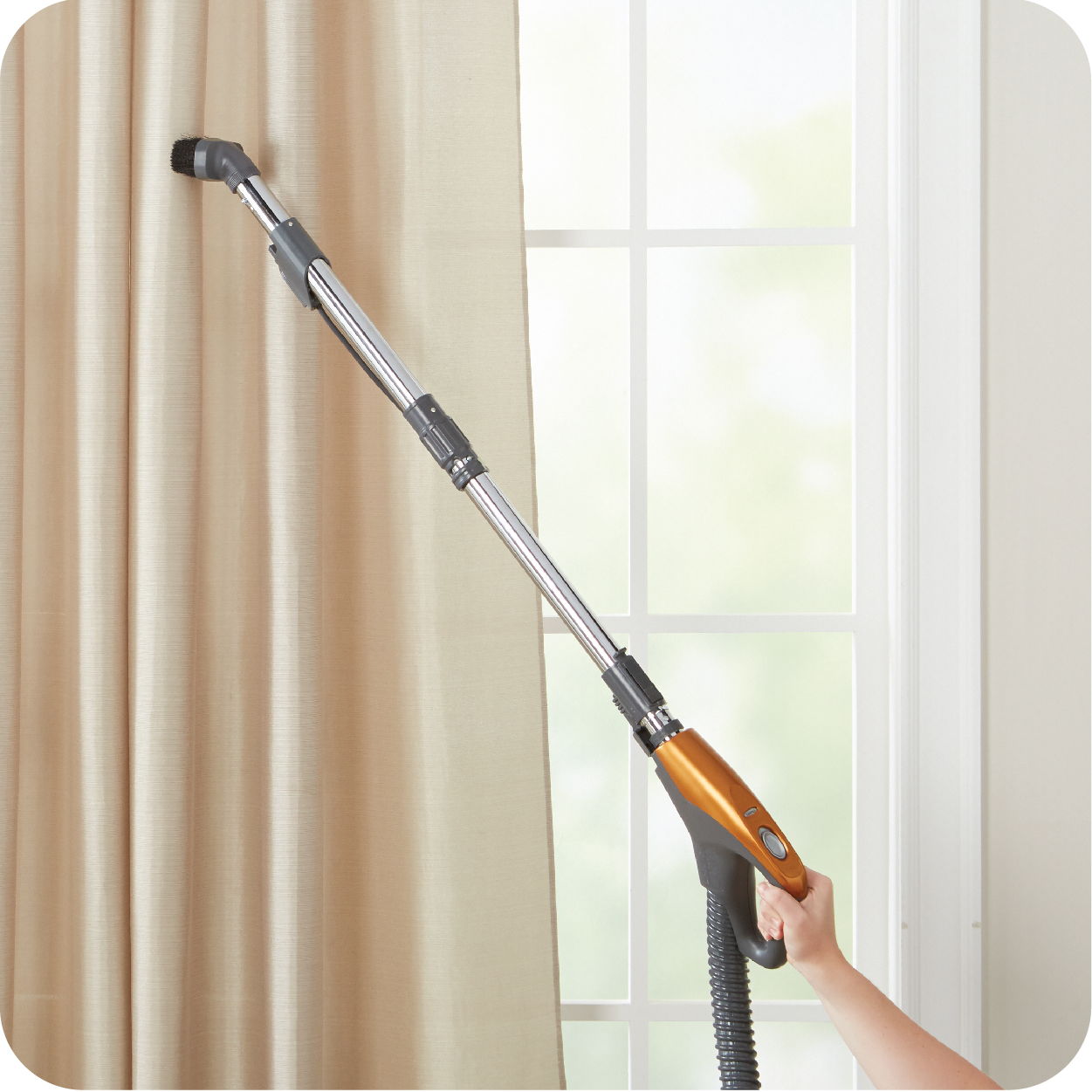 Person using a vacuum attachment to clean curtains.