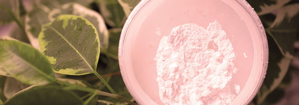 A pink container with white powder surrounded by green leaves.