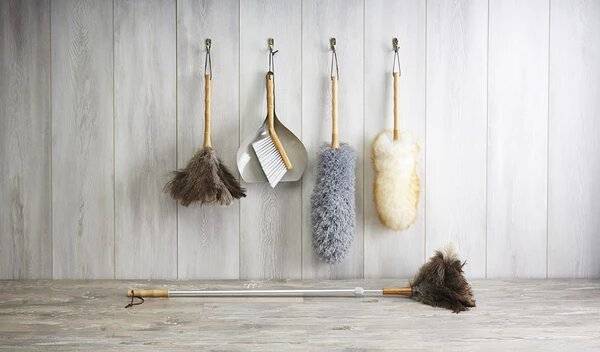 Dusters and a dustpan and brush hanging on a wall, and one on the floor.
