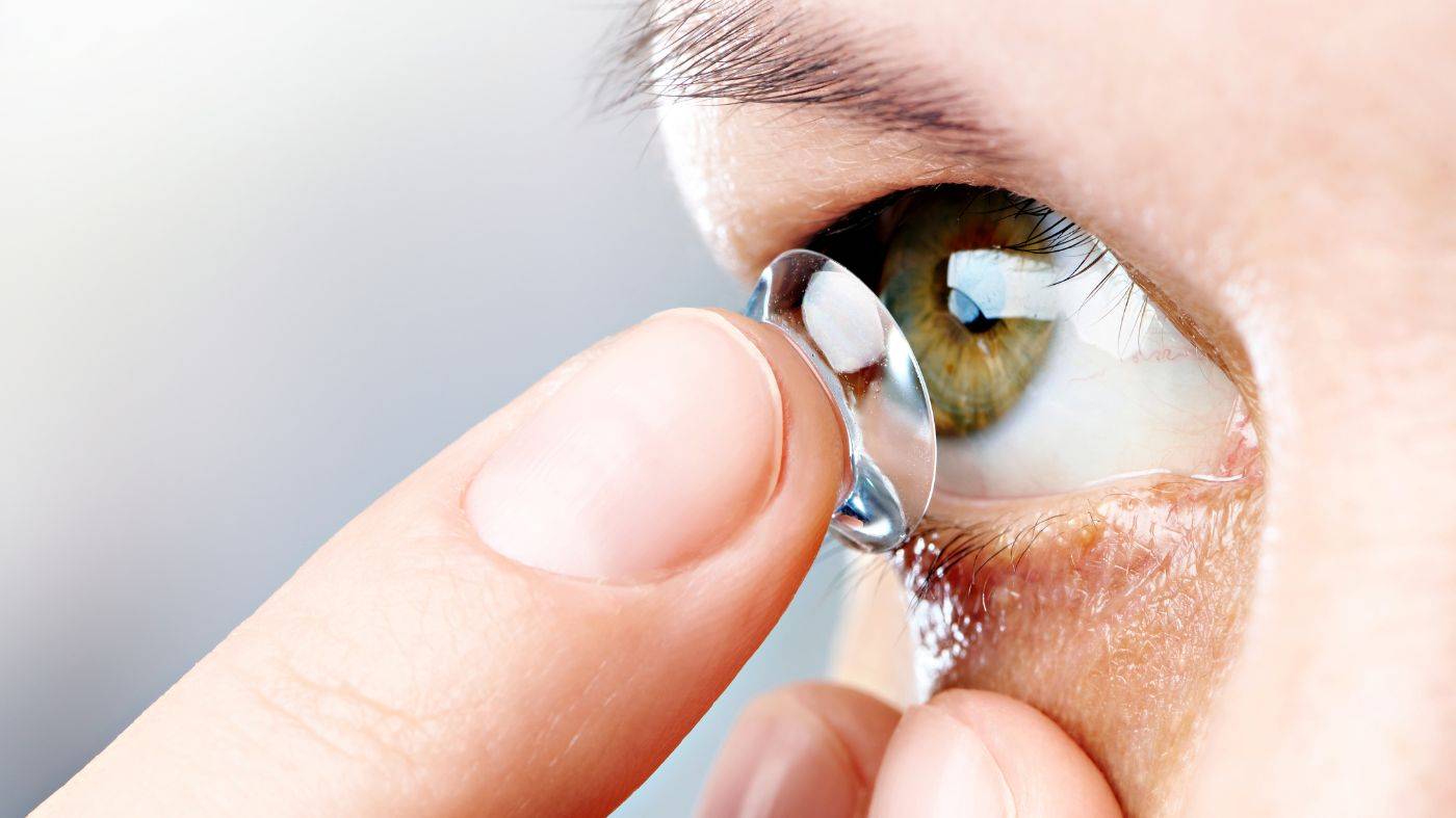 Finger holding a contact lens and inserting to eye