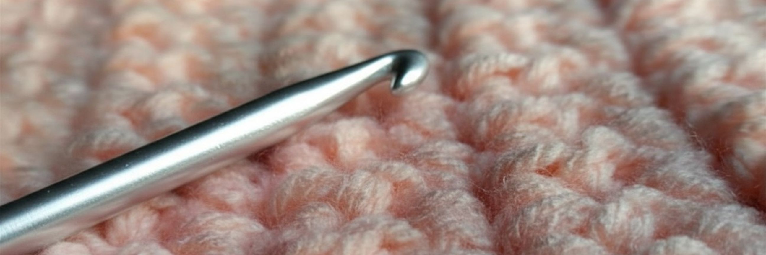 Banner, das eine Häkelnadel auf einem gehäkeltem Textil zeigt.