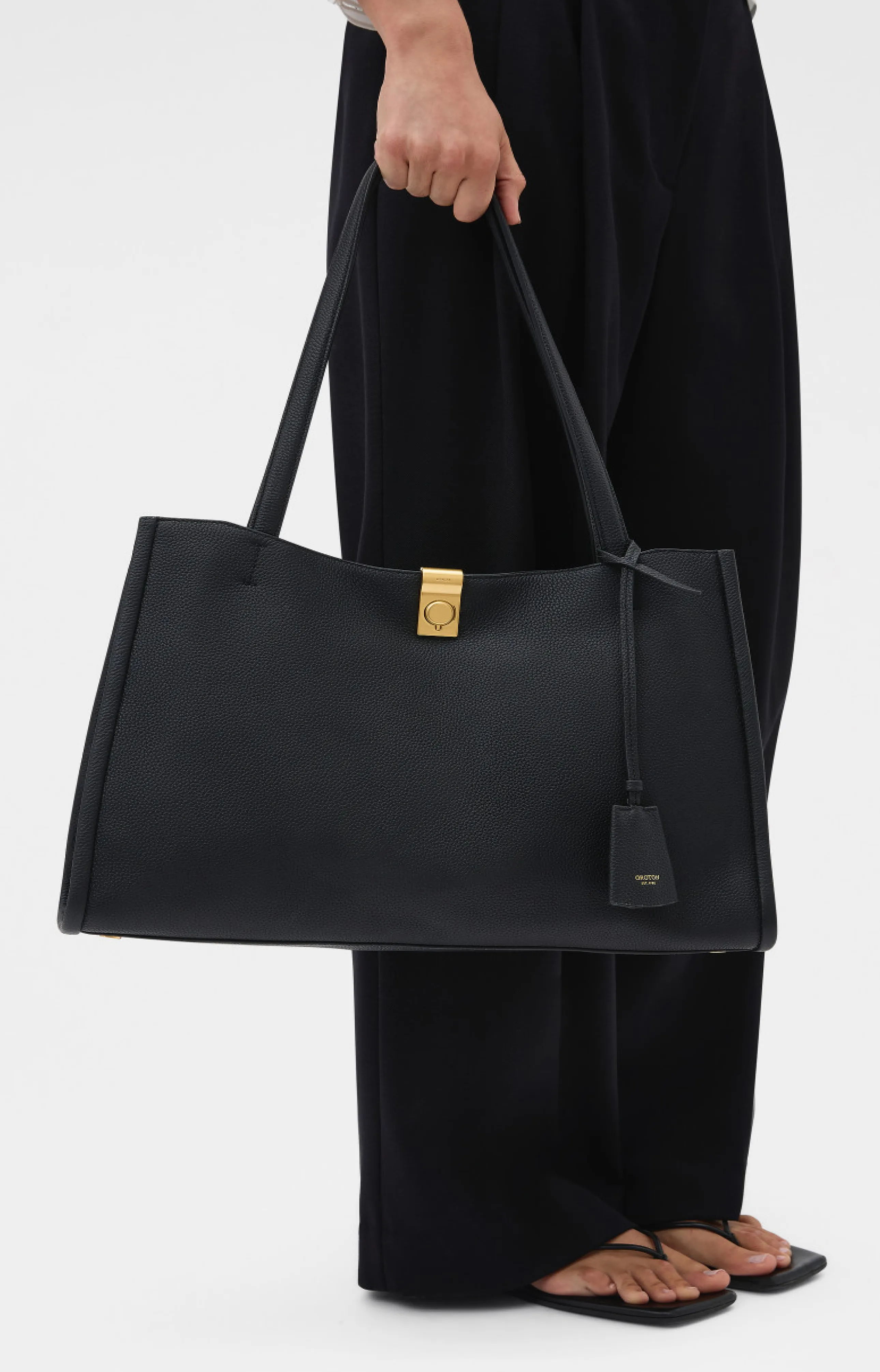 A person holding a large black handbag with a gold clasp.