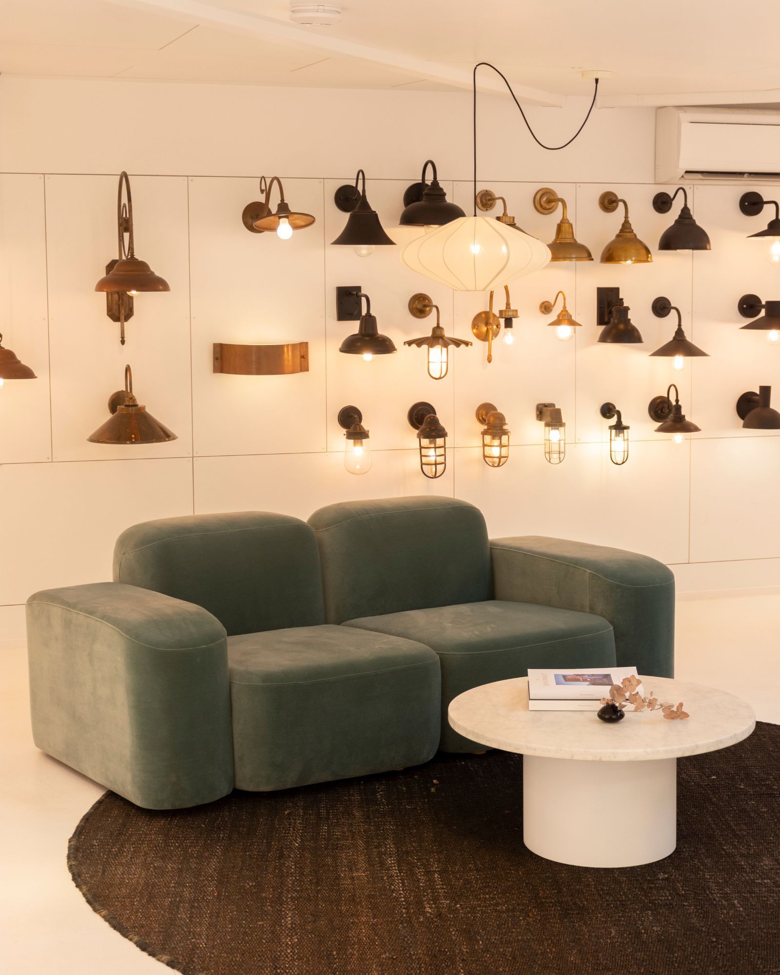 Modern showroom with green sofa, round table, and various light fixtures.